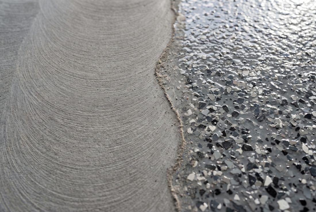 One floor part-way through recoat prep: the left side abraded to a dull matte key with fine sanding arcs, the right side still the original glossy grey flake finish