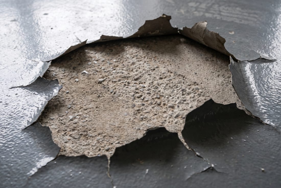 A garage floor coating that has delaminated, with the glossy grey film torn away to expose porous bare concrete underneath