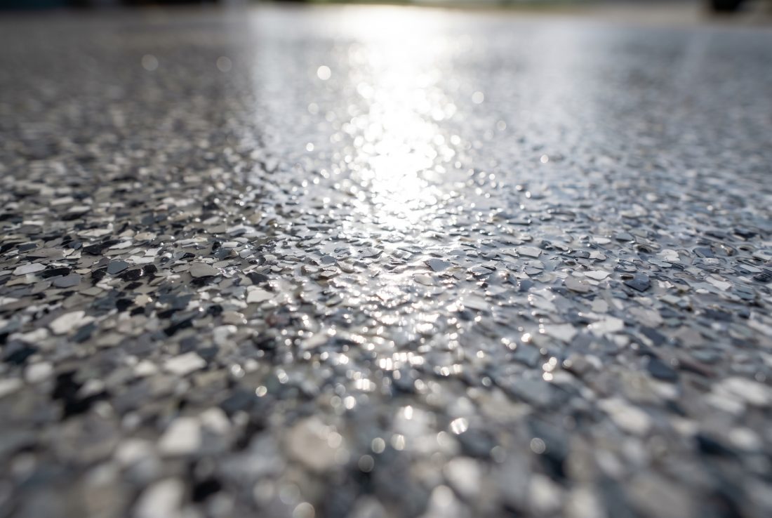 Randomly broadcast gray and charcoal flake under a clear polyaspartic topcoat, the irregular chip pattern that lets a patched area blend in
