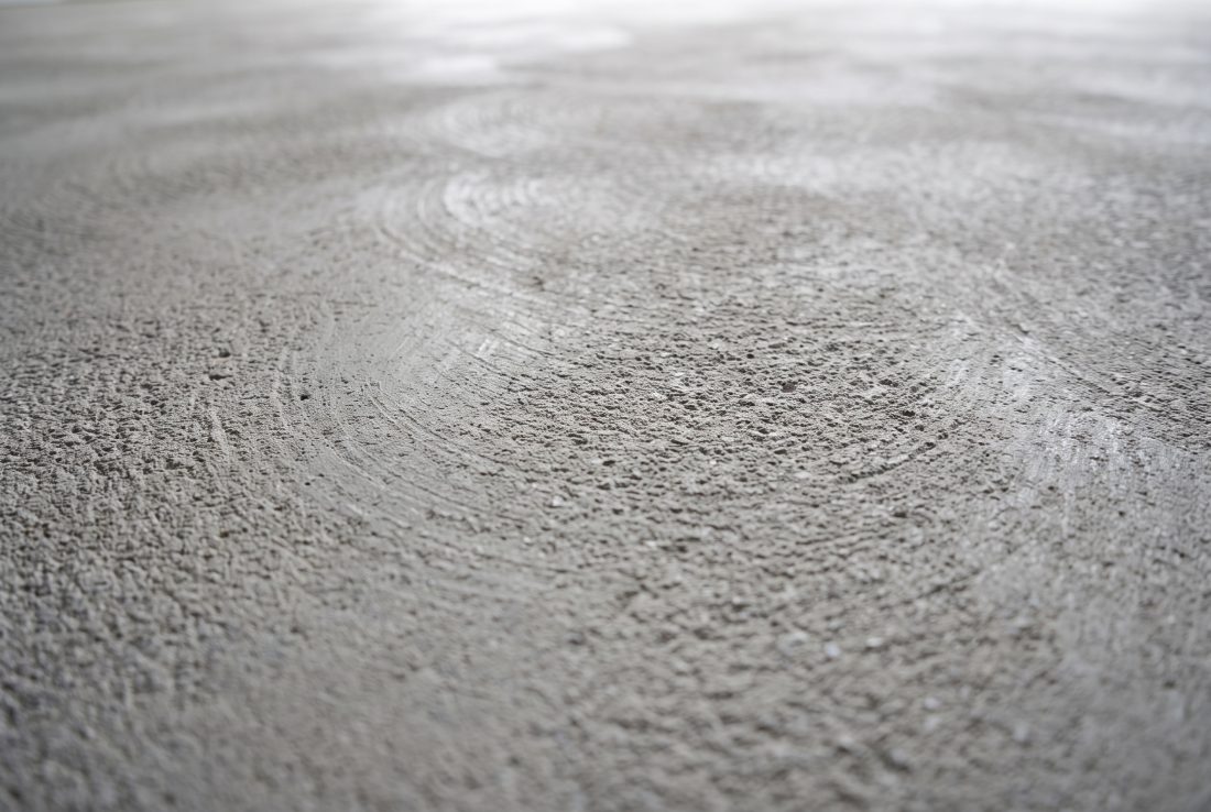 Diamond-ground garage slab showing the open concrete profile a coating keys into, with the shallow dish of a floor drain in the foreground