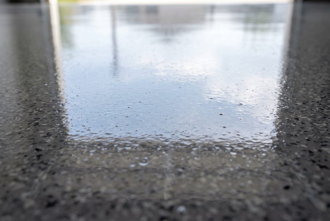 Freshly applied clear topcoat curing over flake on a large concrete floor, with the wet edge still visible