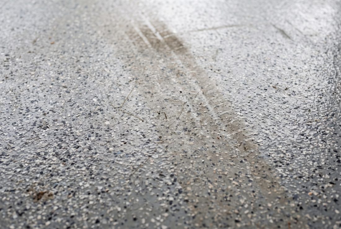 An aged but fully intact flake garage floor coating with a faint dulled tire path crossing the otherwise glossy surface
