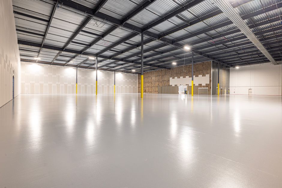 Freshly coated light gray commercial warehouse floor with yellow safety bollards