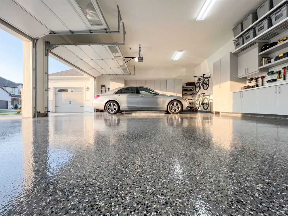 Two-car garage with a gray flake polyaspartic floor coating and a silver sedan parked inside