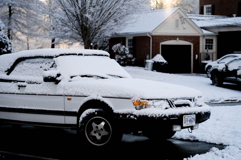 Snow-covered car parked outside a brick garage after a winter storm